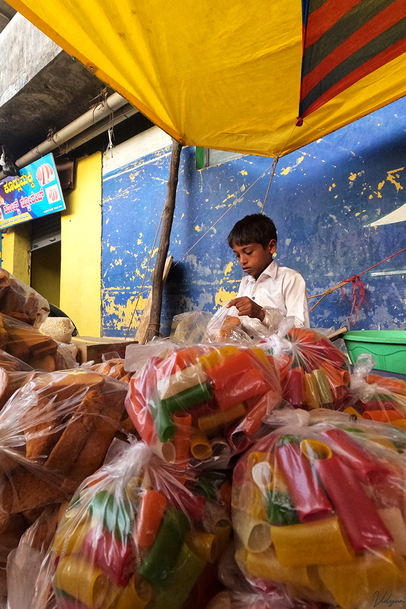 A boy is under a yellow plastic tent with bags of colorful fryums in the forground