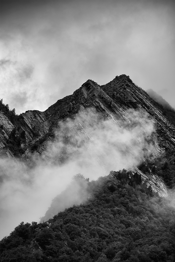 A black & white image of a mountainous region with some fog also in the frame