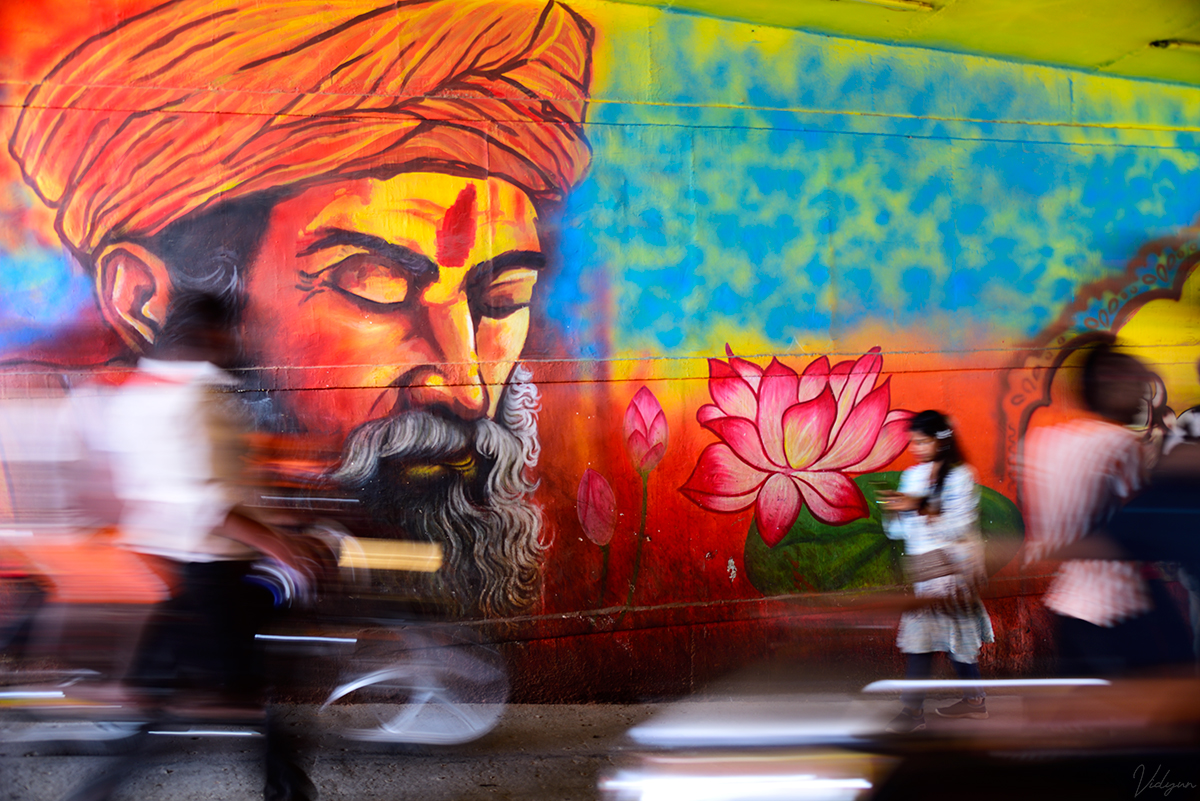 A long exposure image of a painting of a saint on the road with the trails of a few vehicles in the foreground