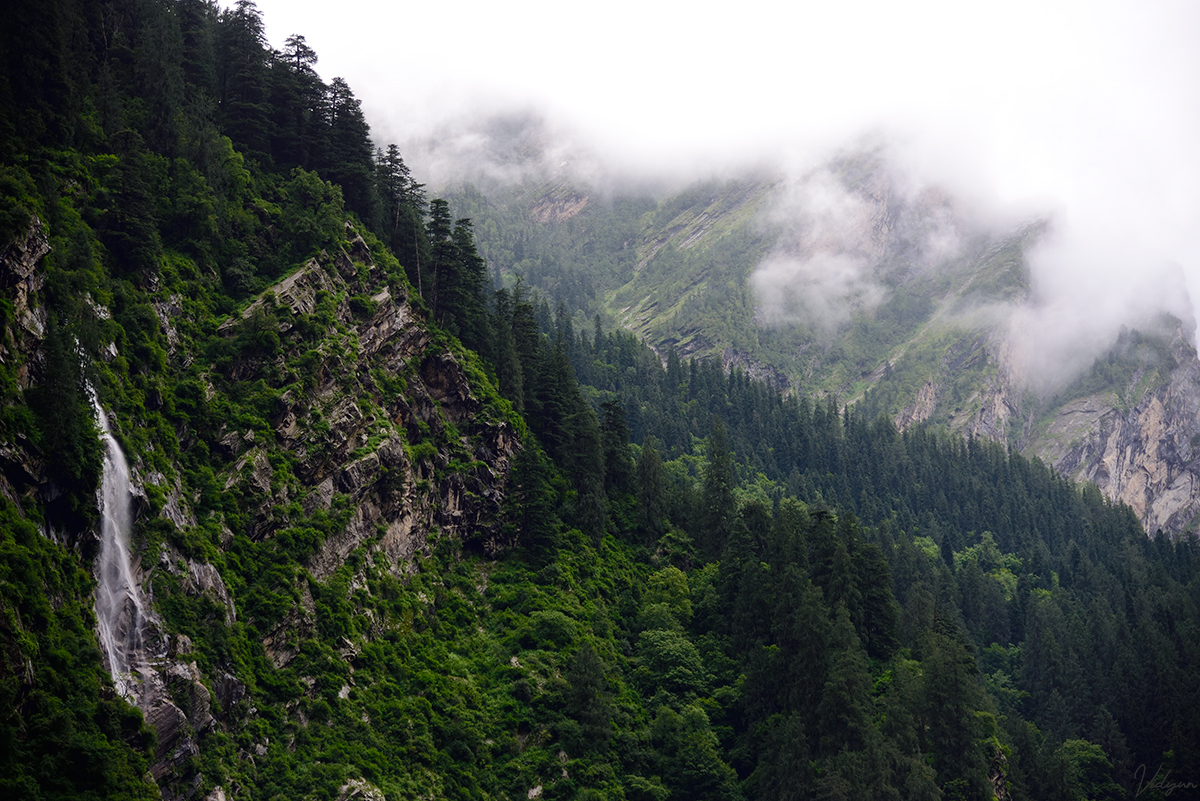 This is a landscape image of a mountain range with a waterfall in the left side and some mountains covered with mist in the background